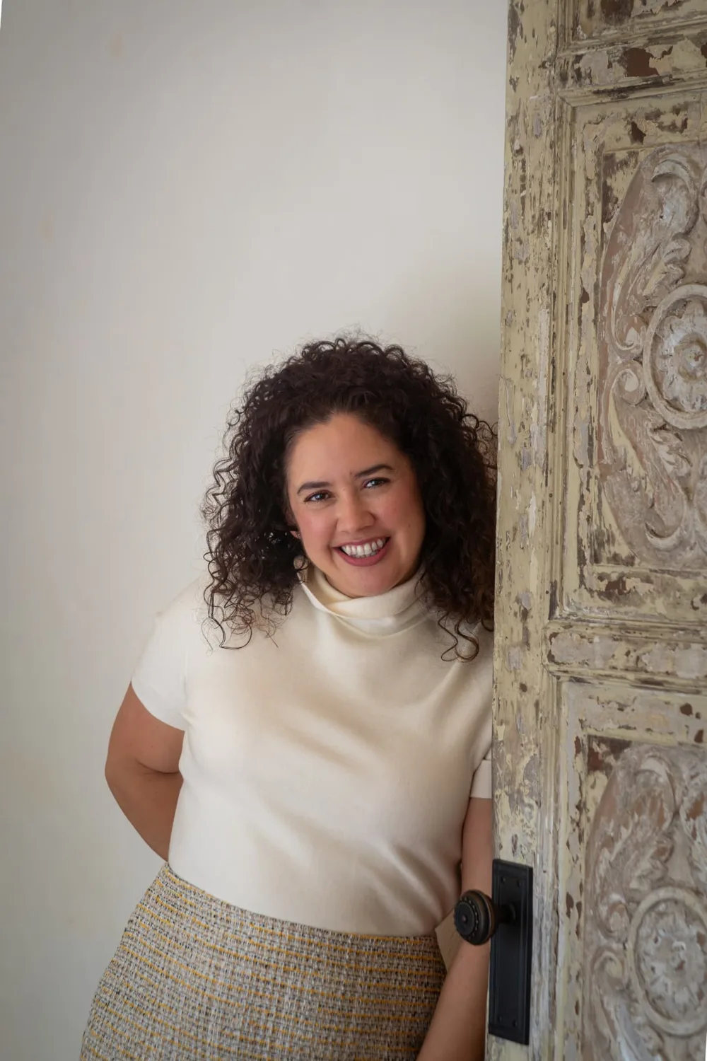 Mayte Villaburu, founder of Dear Ladybug, smiling beside a carved wooden door